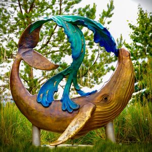 Christina Demetro with Aurora Sidney-Ando Whale Song 5.5 ft high x 7 ft long x 3.5 ft wide. Mountain View neighborhood, Anchorage, AK - awarded twice in recent years as "The Most Diverse Neighborhood in the Nation." A wave splashes over the arched tail of a humpback whale. In an abstract way, the three streams of salmon suggest a stylized peace symbol in the middle. Also, the whale's fins and tail have silhouettes of Alaskan animals, which the viewer can discover upon closer look. Demetro sculpted the front sides of the model and large bronze, while artist Sidney-Ando sculpted the backsides, along with 94 Alaskan children co-sculpting from Mt View Boys and Girl's Club and Wonder Park Elementary School. The students also placed blue “Pledges of Peace” handprints on stones to create a ripple of ocean water around the base. They each pledged to do one good deed for their neighborhood.